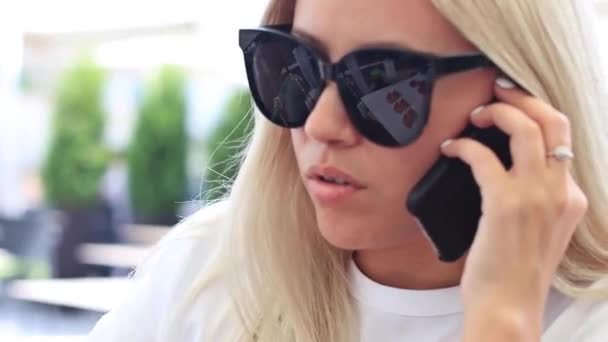 Junges blondes Mädchen telefoniert mit Handy in Straßencafé. — Stockvideo