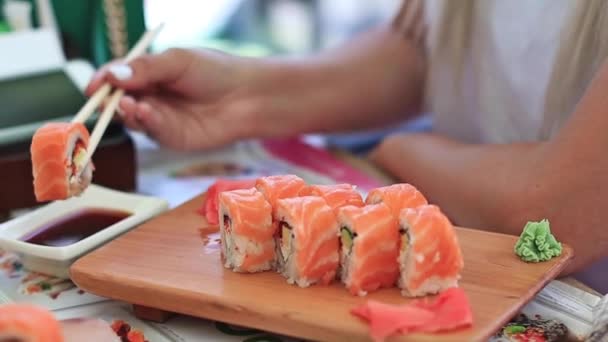 Lassított élelmiszer-felvételeket. Japán étterem tengeri ételek menüt. Egészséges táplálkozás, táplálkozás, diétázás fogalma. Closeup shot a női kéz pálcika dunks stílusosan meghatározott sushi meghatározott szójaszósz — Stock videók