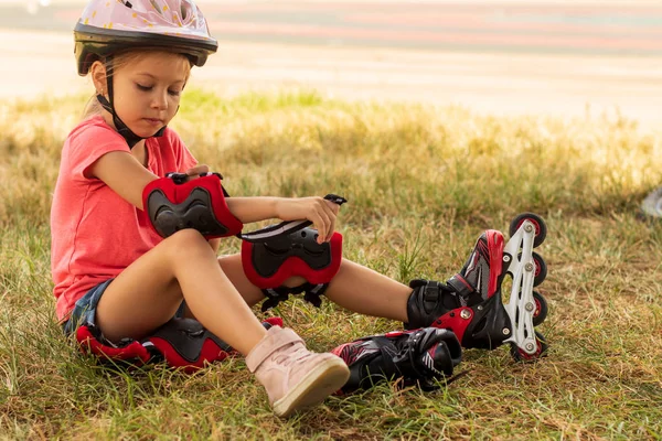 小さな女の子はローラースケートのための保護を置く — ストック写真