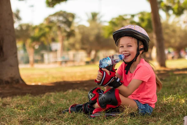 Маленька дівчинка в роликових ковзанах питна вода в парку — стокове фото