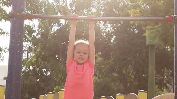 Malá holčička vytáhne na hrazdě v létě městský park. — Stock video