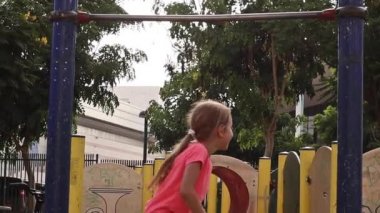 parkta oyun alanında oynayan kız, yatay bar tırmanmaya çalışıyor