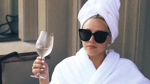 Krásná blondýnka v bílém županu a sluneční brýle požívající sklenici šampaňského — Stock video