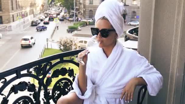 Mujer joven en balcón o terraza en albornoz blanco y toalla y beber champán de cristal — Vídeos de Stock