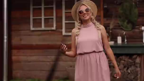 Jonge stijlvolle vrouw staat naast een oud houten huis op de achtergrond — Stockvideo