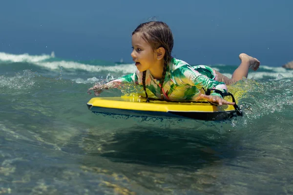 Blond little girl on surfboard floating against the water flow
