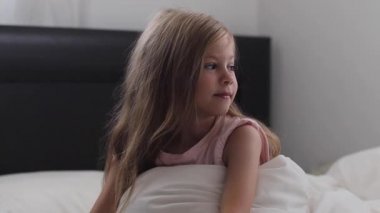 çocuk bir gülümseme ve sevinç ile uyanır. Bebeği yatakta yudumluyor. Beyaz yatakta günaydın.