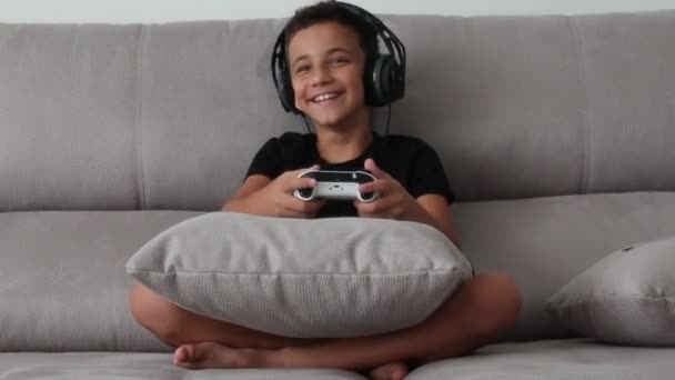 Boy smiling and having fun playing a video game with controllers on a couch. — Stock Video