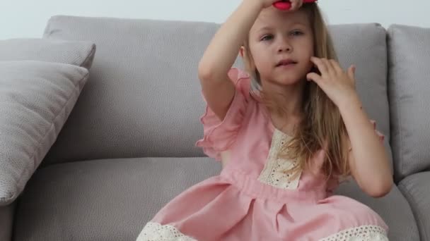 Мила маленька дівчинка розчісує її світле волосся пензлем — стокове відео