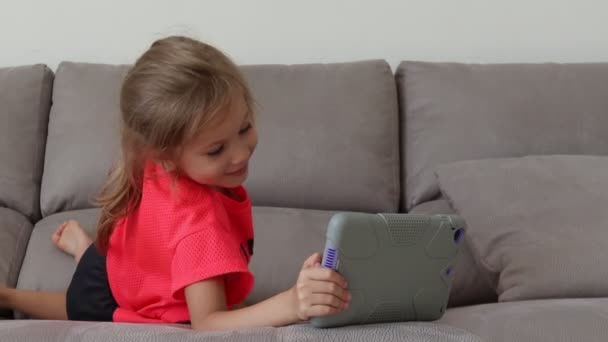 Chica feliz jugando con la tableta en casa. Divertido niño encantador se divierte en la habitación — Vídeos de Stock