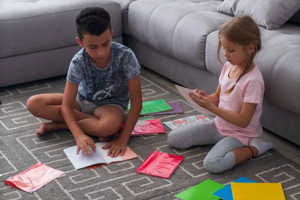 Gerichte jongen en meisje in Casual kleding zetten covers op nieuwe copybooks terwijl zittend op de vloer — Stockfoto