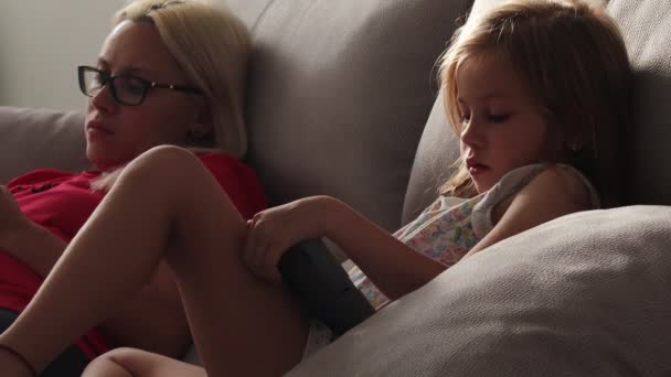 Mamá y su hija están sentadas, mirando la pantalla de la tableta y el teléfono — Vídeos de Stock