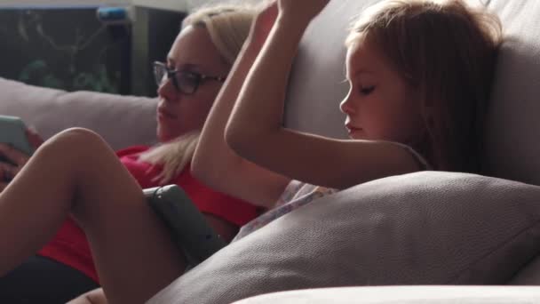 Mamma e figlia sono sedute, guardando lo schermo del tablet e del telefono — Video Stock