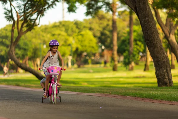 Маленька дівчинка носить свою маленьку сестру-братівню на дитячому велосипедному сидінні в парку — стокове фото