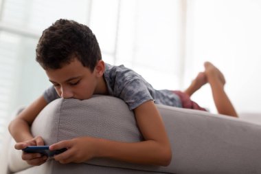 Çocuk kanepede yatıyor ve akıllı telefonda oyun oynuyor.
