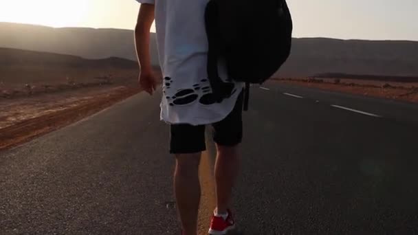 Wanderer nebo Samoter kráčí po asfaltové silnici s batohu na zádech při západu slunce — Stock video