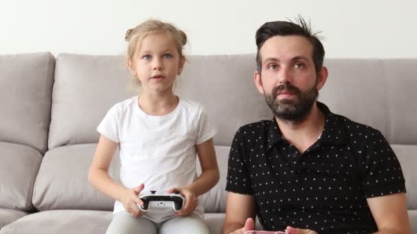 Otec a malé dítě hrají na gauči doma videohru a stiskávají tlačítka na pákového ovladače. — Stock video