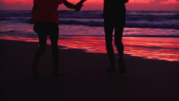 Silhouetten von Kindern laufen bei Sonnenuntergang Händchen haltend am Meer entlang. — Stockvideo