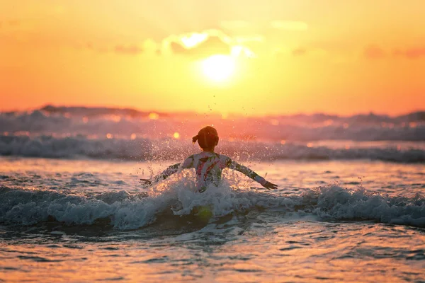 Menina no pôr do sol pulando sobre as ondas — Fotografia de Stock