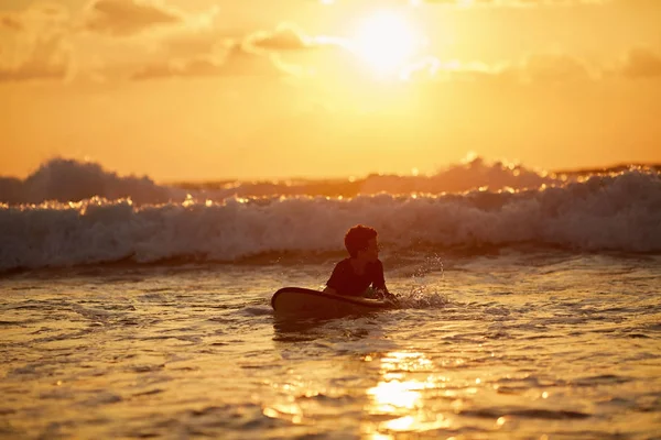 Adolescente cualificado montando tabla de surf y equilibrándose a lo largo del mar ondulado al atardecer vibrante . —  Fotos de Stock