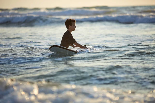 アジアの熱帯ビーチでサーフィンをしている10代の少年。波の上のサーフボード上の子供 — ストック写真
