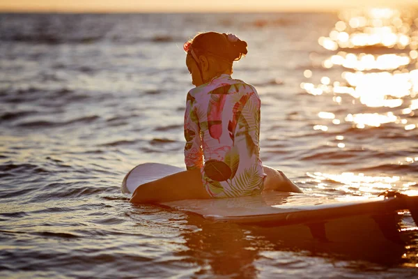 Surf e férias. Férias na praia. Menina relaxada sentada na água com prancha desfrutando do pôr do sol — Fotografia de Stock