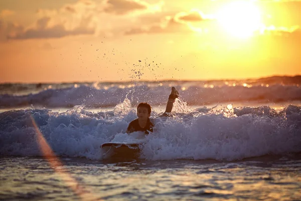 Carefree boy surfing at wave at colourful sunset — Stock Photo, Image