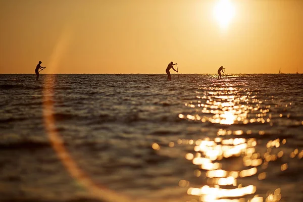 Três pessoas remando em uma prancha de surf para o horizonte no mar aberto belo pôr do sol cênico — Fotografia de Stock