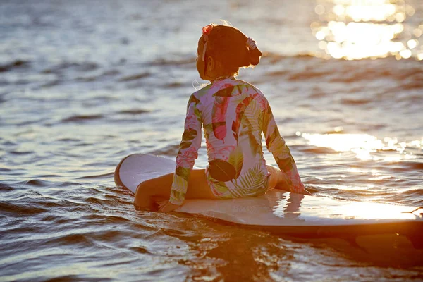 Relaxado jovem sentada na prancha de surf apreciando o pôr do sol — Fotografia de Stock