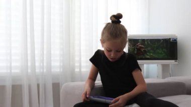 Süt dişi olmadan ağzı açık okul öncesi kız portresi. Evde tabletle oynayan mutlu kız. Komik güzel çocuk odada eğleniyor