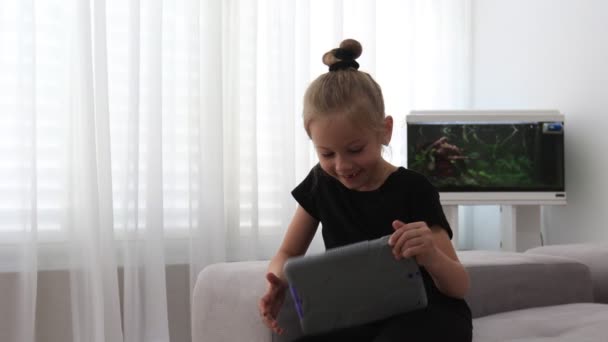 Маленька мила дівчинка портрет посмішки без одного переднього молока зуба дивиться в сірий планшет — стокове відео