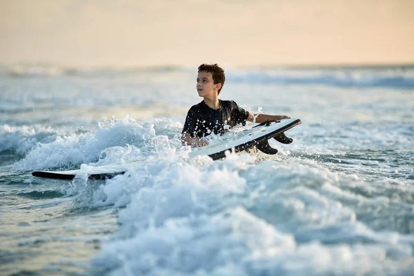 Szörfös fiú az óceánban naplementekor vagy napkeltekor. Szörfös és óceán — Stock Fotó