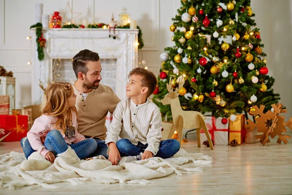 Pai e seus dois filhinhos sentados na chaminé da lareira no tempo da véspera de Natal — Fotografia de Stock