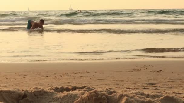 Niño está corriendo y saltando al agua en una playa de mar al atardecer 4k — Vídeos de Stock