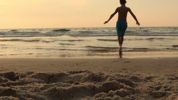 Niño está saltando en una playa al atardecer. Hiperactivo chico correr y saltar en playa arena sonriendo . — Vídeos de Stock