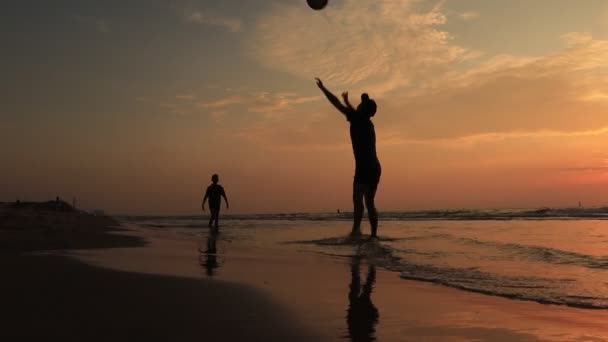 Padre e figlio giocano a frisbee insieme in pantaloncini al tramonto del mare. Gente di silhouette che gioca con frisbee sulla spiaggia retroilluminata dal sole estivo — Video Stock