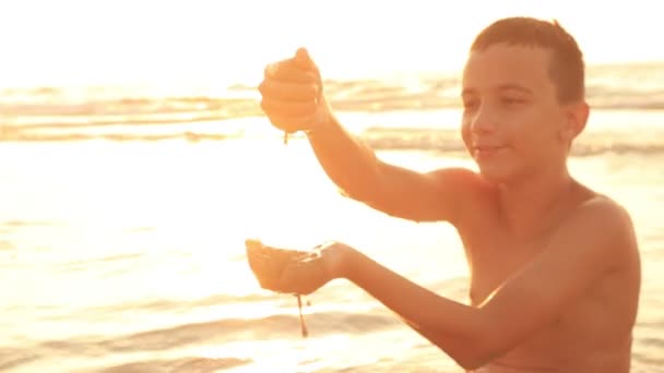 A wonderful view of a nine-year-old boy who builds a sandy fortress on a seacoast on a sunny day in slow motion. The skyscape is beautiful and inspiring. The sea surface sparkle in a splendid way. — Stock Video