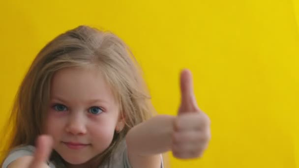 Sonriente niña muestra los pulgares hacia arriba gesto sobre fondo amarillo aislado — Vídeos de Stock