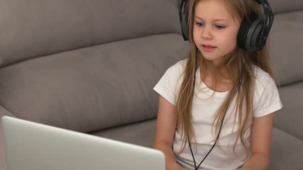 ヘッドフォンに長い髪のブロンドの女の子コンピュータの前に座って歌を歌う — ストック動画