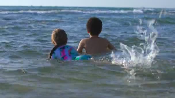 Щасливий хлопчик і дівчинка грають у морській воді влітку в теплий сонячний день — стокове відео