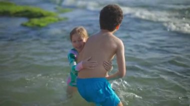 Çocukların soğuk denizi yüzme konusunda tereddütleri var. Çocuklar deniz kıyısında oyun oynuyorlar. Yüksek kaliteli FullHD görüntüler