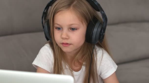 긴 머리에 헤드폰을 낀 금발의 어린 소녀는 컴퓨터 앞에 앉아 노래를 부른다. 고품질 4k 필름 — 비디오