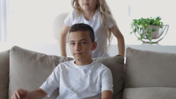 Petite sœur et frère caucasien en T-shirts blancs et cheveux blonds assis à la table. soeur câlins frère et baisers — Video