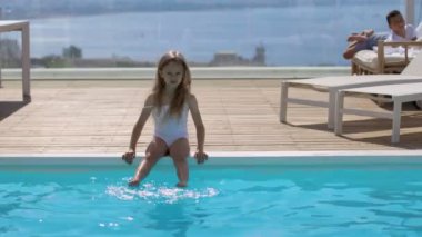 Havuzun yanında beyaz mayo giymiş küçük bir kız.