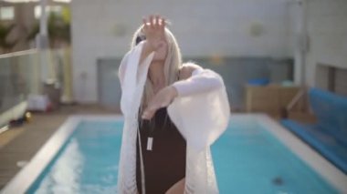 Yüzme havuzunun yanında dans eden siyah elbiseli ve güneş gözlüklü genç, ince seksi pozitif kadın portresi.