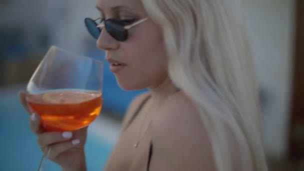 Красивая девушка пьет алкогольный коктейль у края бассейна. Высококачественные FullHD кадры — стоковое видео