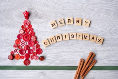 Ahşap harflerle yazılmış el yapımı kırmızı Noel ağacı. Altta yeşil kurdele ve tarçın çubukları olan beyaz ahşap arka planda mutlu noeller.