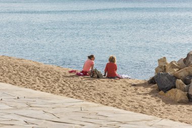 İspanya, Blanes - 16 Eylül 2017: İki kız sahilde suya yakın oturan ve konuşmak
