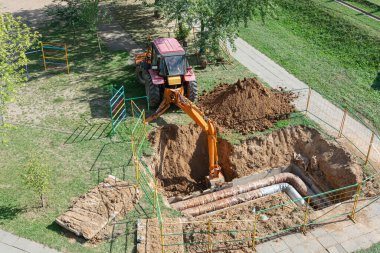 Minsk, Belarus - 09 / 12 / 2018: Traktör patlamış bir ısıtma borusunu tamir etmek için çukur kazıyor