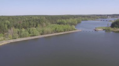 Bir orman arka planında ve bir baraja karşı suyun üzerinde uçan insansız hava aracı. Düşük irtifa, su üzerinde dalgalanmalar.